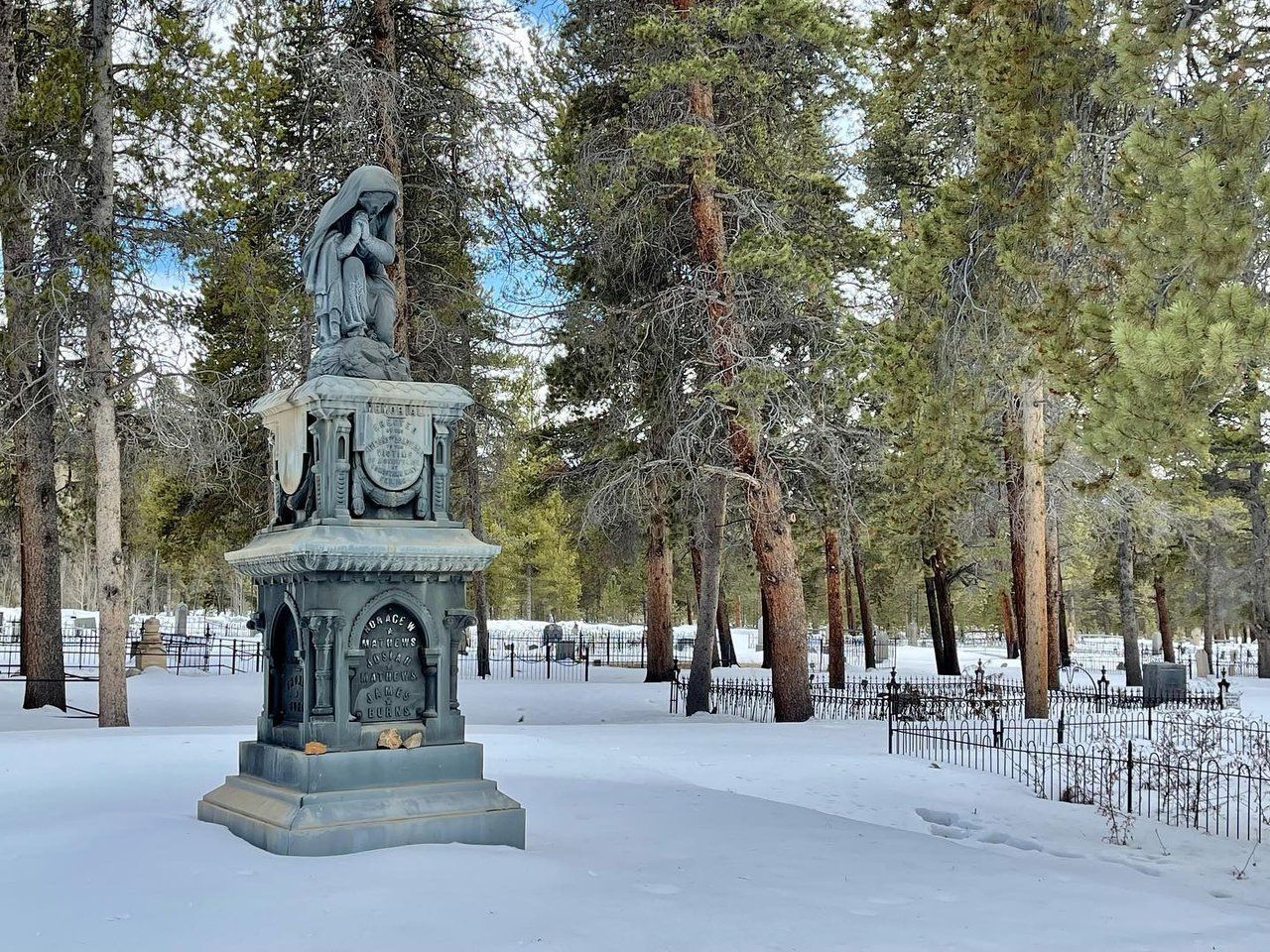 Statue at Evergreen Cemetery surrounded by fir trees and snow