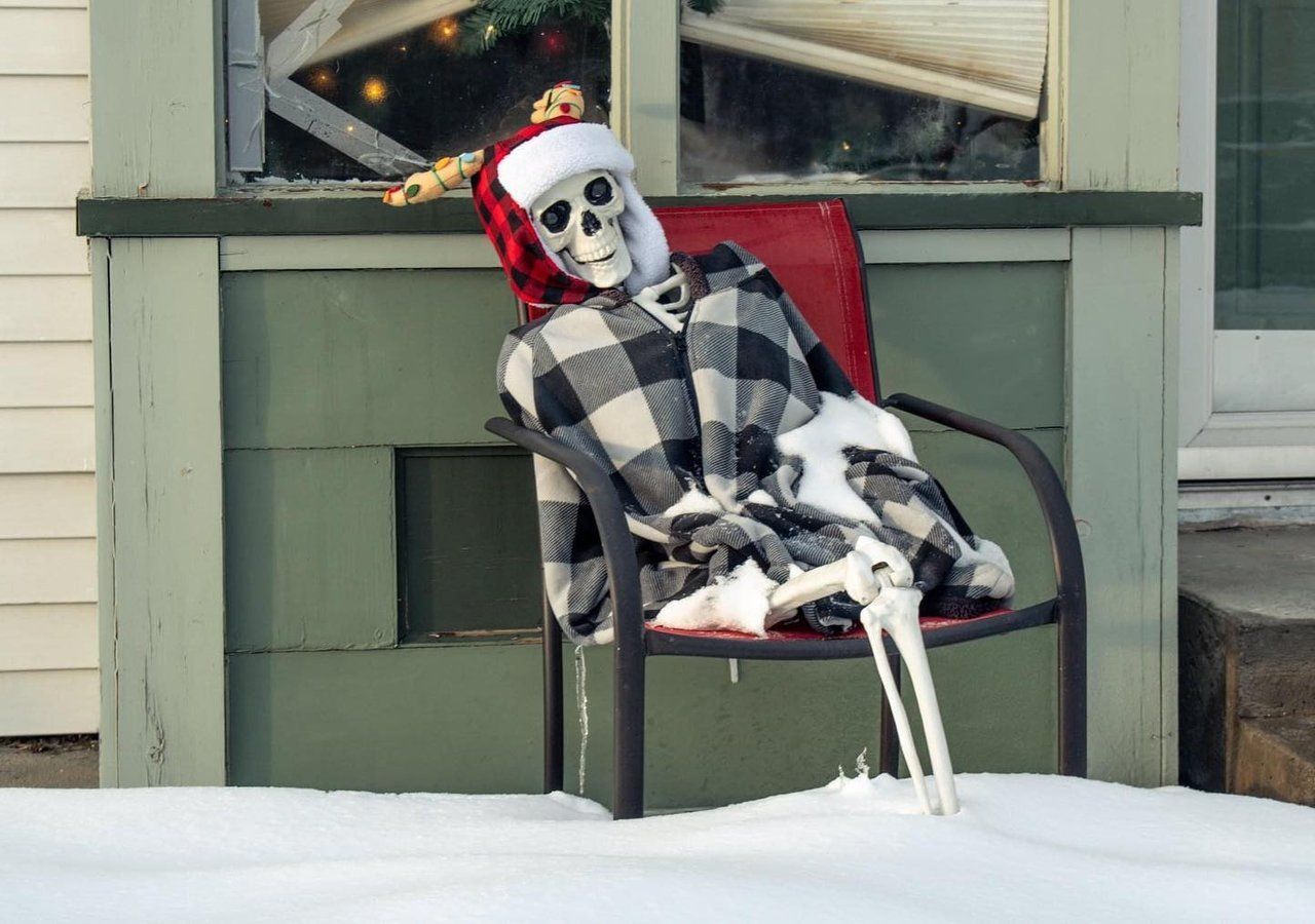 Halloween skeleton sitting in a chair, wrapped in a blanket, in snow by @adesri_photography